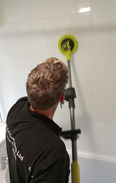 A person using a wall-mounted cleaning tool to scrub tiles.